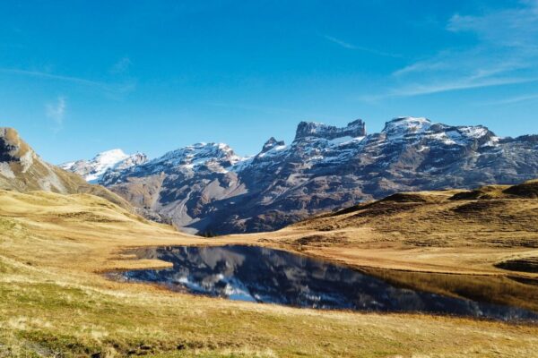 Foto von kleinem Bergsee bei Melchsee-Frutt mit Spiegelung der Berge im See, Wanderung zum Engstlensee. Herbstliche Färbung der Wiese im Vordergrund.