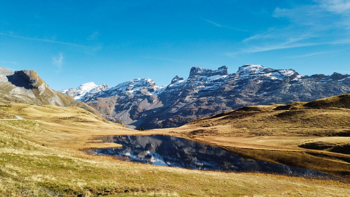 Foto von kleinem Bergsee bei Melchsee-Frutt mit Spiegelung der Berge im See, Wanderung zum Engstlensee. Herbstliche Färbung der Wiese im Vordergrund.