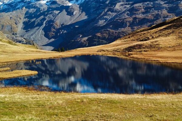 Foto von kleinem Bergsee bei Melchsee-Frutt mit Spiegelung der Berge im See, Wanderung zum Engstlensee. Herbstliche Färbung der Wiese im Vordergrund.