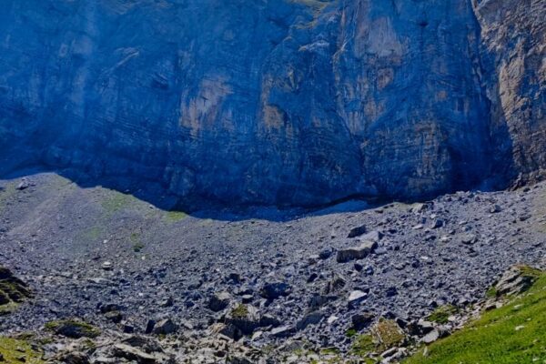 Foto vom türkisen Tschalmeten-Seeli beim Schwarzgrätli mit hohen Felsen im Hintergrund.