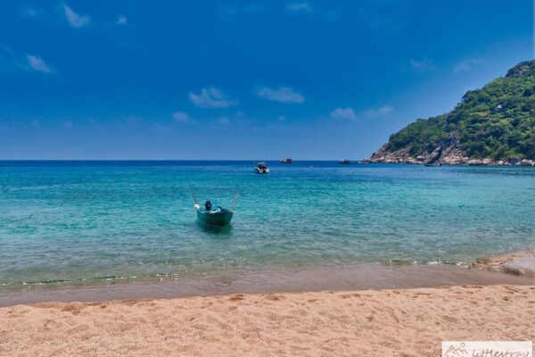 Strand mit türkisblauem Wasser und vier Booten im Wasser.