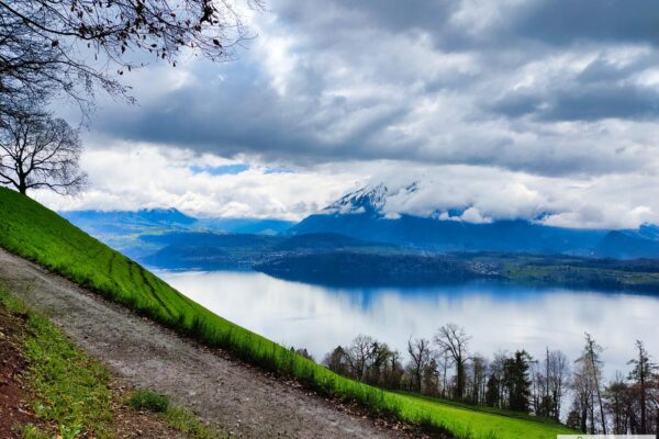 Blick auf den Thuner See vom panoramaweg oberhalb Oberhofen, Wolken verdecken die Berge teilweise.