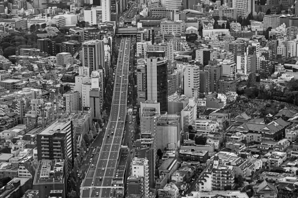 Schwarz-weiss Aufnahme einer breiten Strasse mit Hochhäusern in Tokio vom Mori Tower aus gesehen (Vogelperspektive)