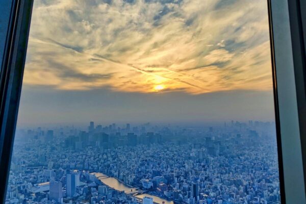 Foto aus einem der Fenster des Skytree, man sieht den Sonnenuntergang, den Sumida River und gelb beleuchtete Wolken.