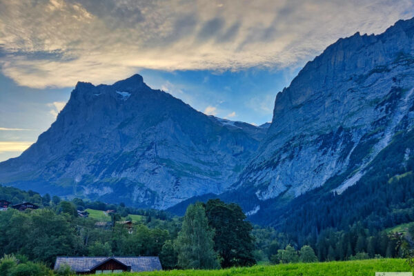 Berge bei Sonnenuntergang mit Wiesen und Bäumen davor.