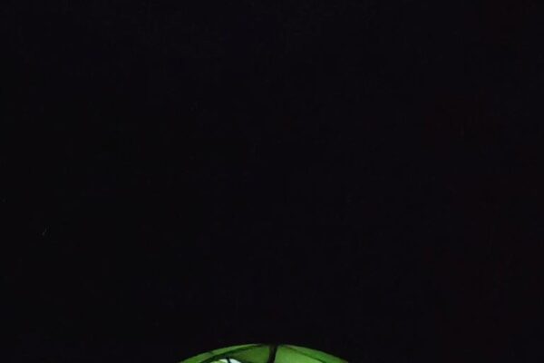 Von innen hell erleuchtetes Zelt und Berge mit Nachthimmel im Hintergrund auf der Alp Oberfeld